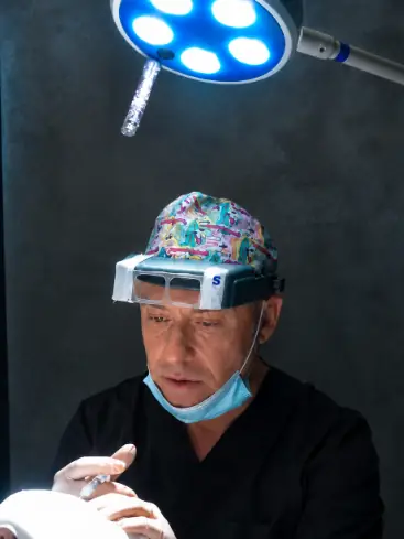 El Dr. Monaco operando en quirofano con lupas de aumento y luz frontal